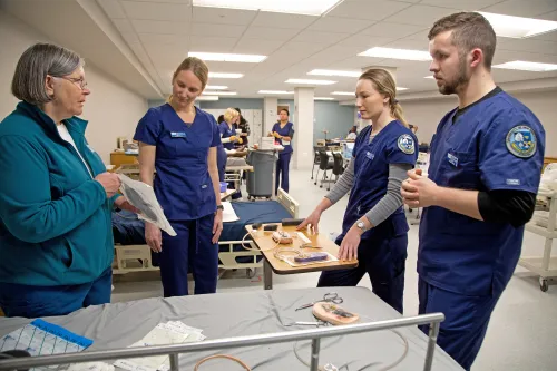 A group of nursing students in dark blue scrubs listen as a professor explains an incision management system