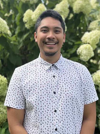 Portrait of Jordan Agabin, smiling in front of flower bush