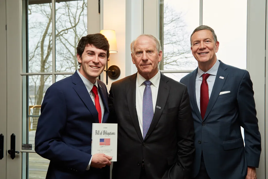 Three men pose for a photo, one is holding a book
