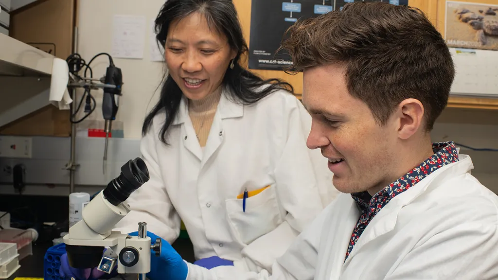 Ling Cao assists a student with a microscope