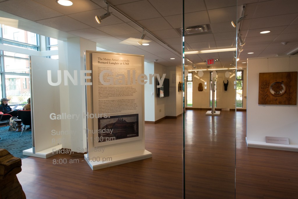 An interior shot of the art gallery on the Biddeford Campus featuring a glass door that says "U N E Gallery." Artwork hanging inside can be seen through the door.