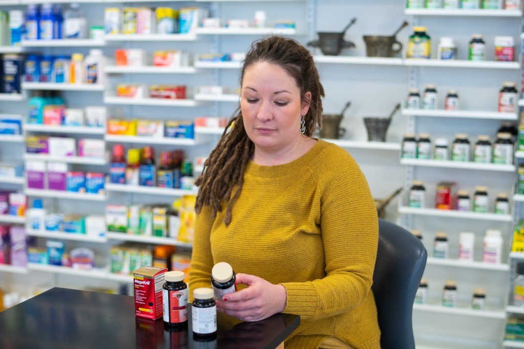 A pharmacy student sits in front of a wall of medicine bottles and is reviewing the ingredients on a pill bottle