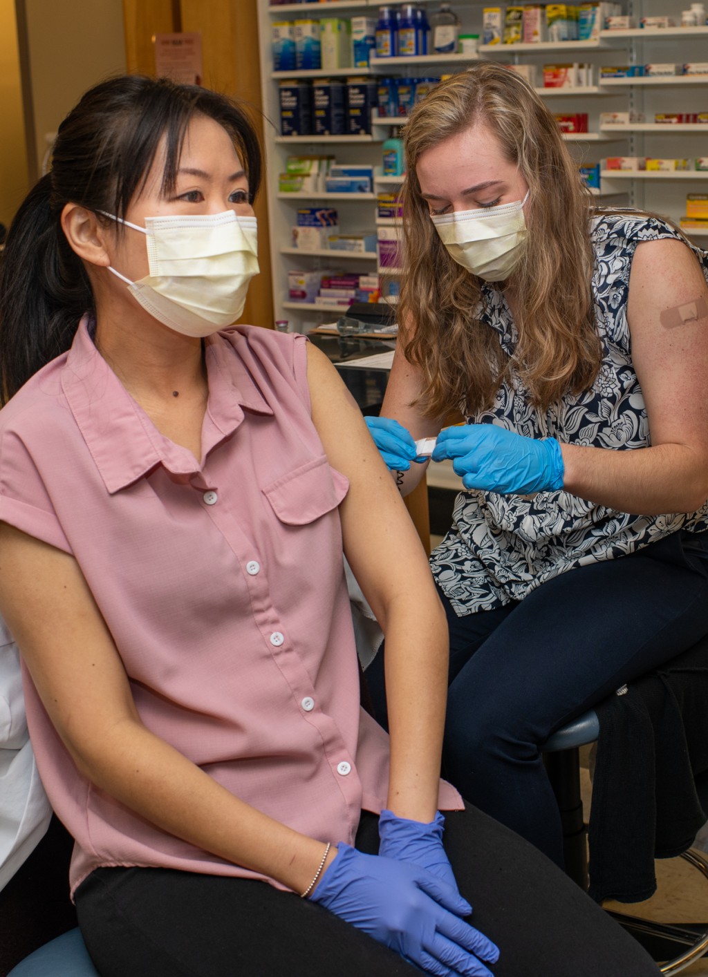 Two pharmacy students are wearing masks and practice giving one another vaccine shots in the upper arm