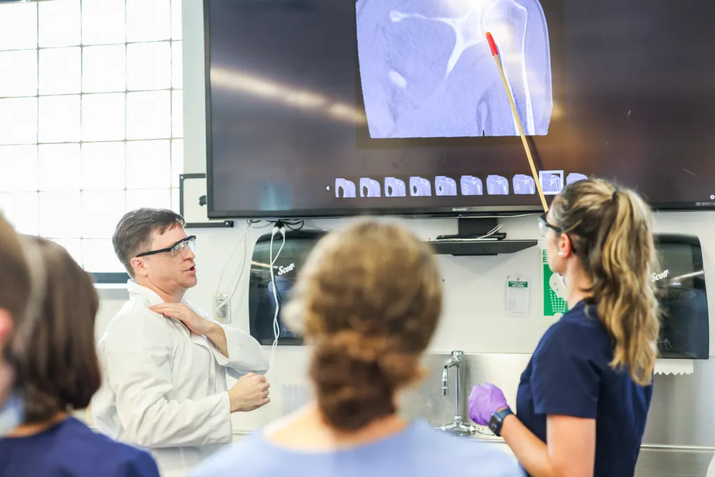 A student points to an anatomical image on a screen in front of their classmates