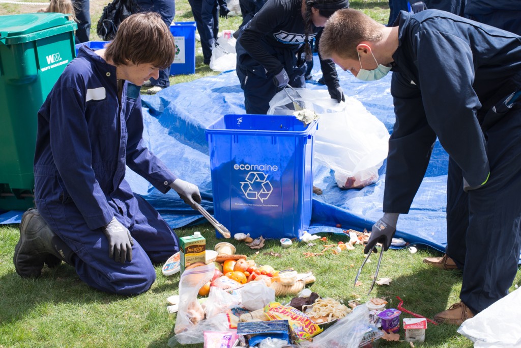 Two students in coveralls are sifting through trash to find items for recycling