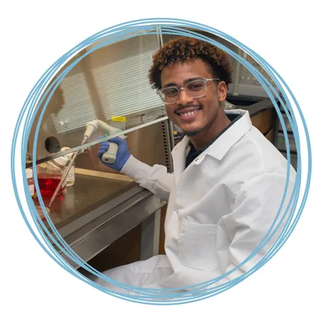 A student wears a white coat as they work in a lab setting for U N E research