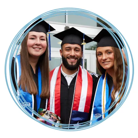 Three students stand together in their academic regalia before their graduation ceremony