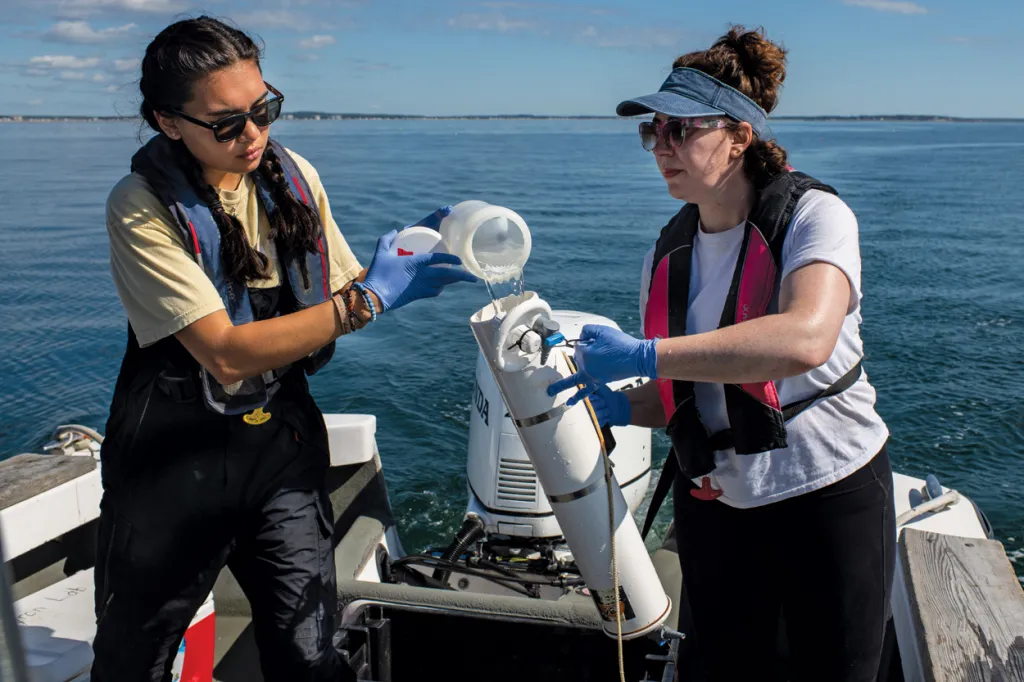 Two marine science students filling a sampling container with ocean water