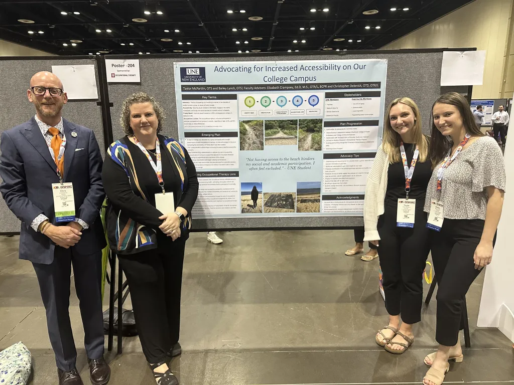 Four UNE researchers pose in front of a poster
