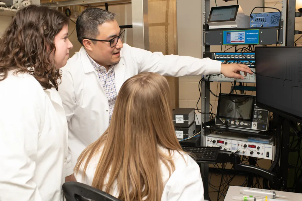 Luis Queme and two students look at a graph on a monitor in his lab