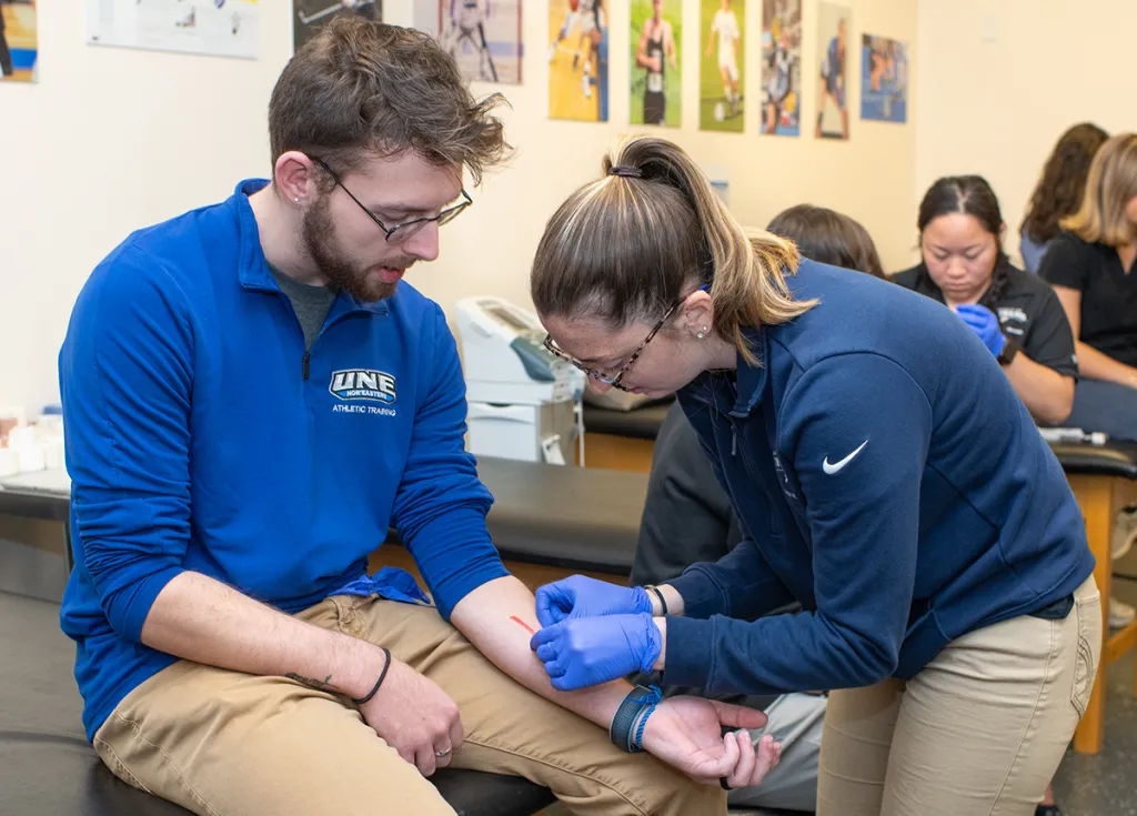 An athletic training student practices mending a wound on another A.T. student