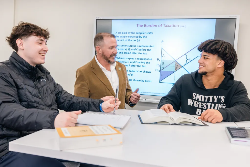 Two Economics students in a discussion with their professor during a class