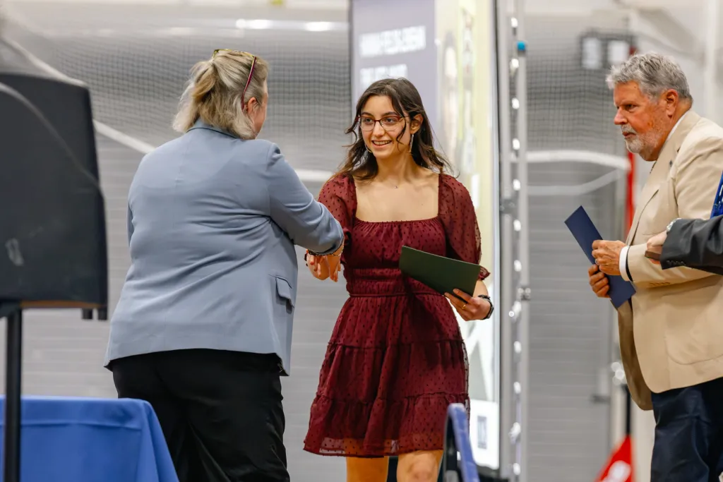Amy Haile shakes hand with a student at University Award Ceremony