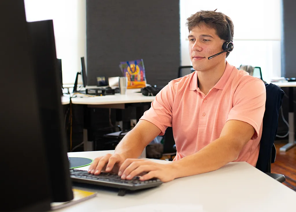 A student wearing a headset at a computer in a business office