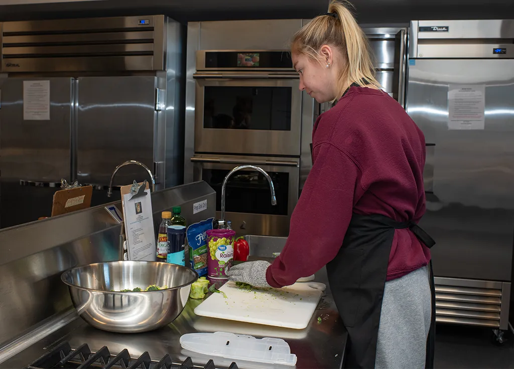 A nutrition student in an apron cuts vegetables in an industrial-style kitchen