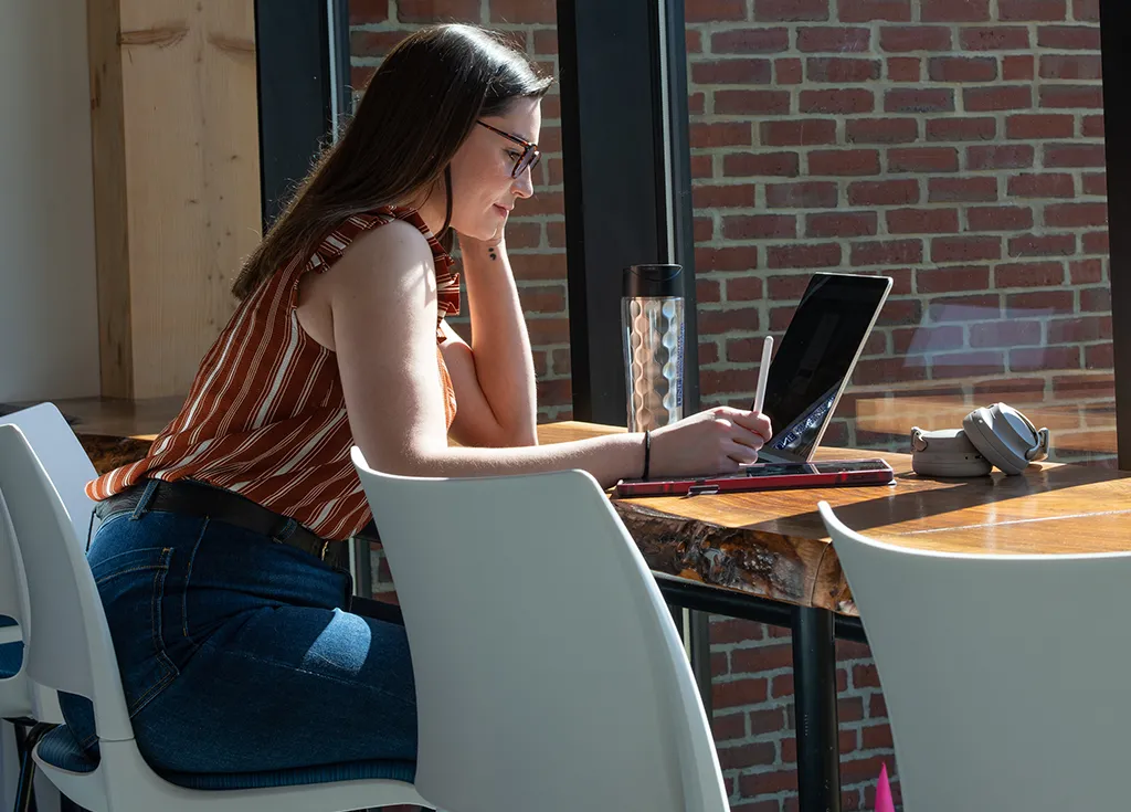A student sits at a long, wooden counter and studies on her laptop
