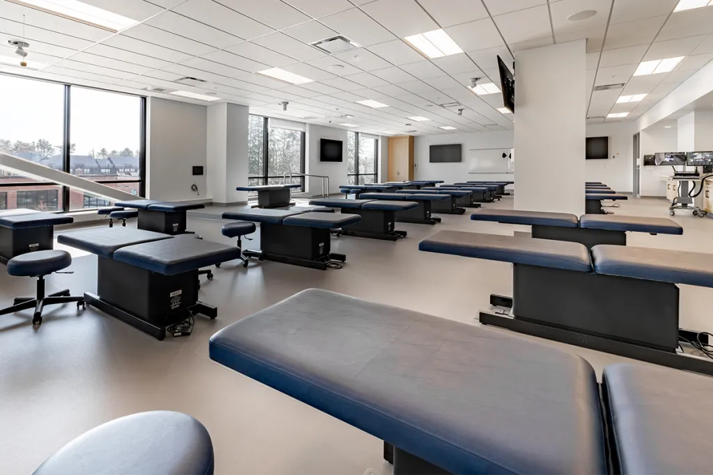 Rows of exam tables in a white room lined by large windows on one side