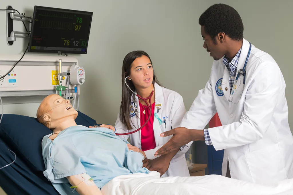 Two C O M students check the vitals on a patient simulator in the Sim Lab