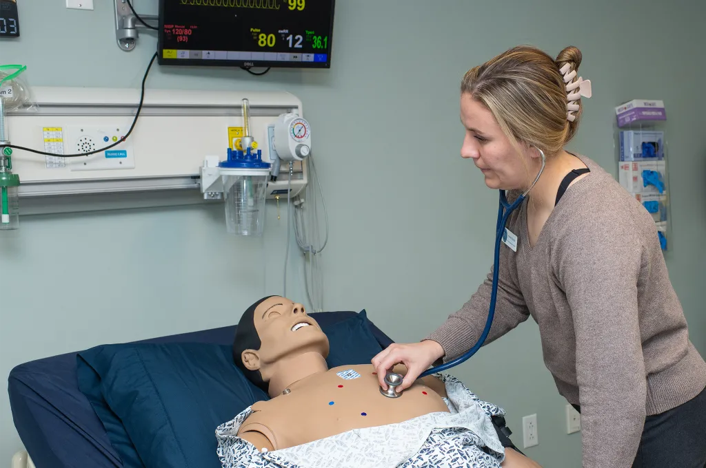 A P A student uses a stethoscope to listen to the cardiac sounds of a patient simulator