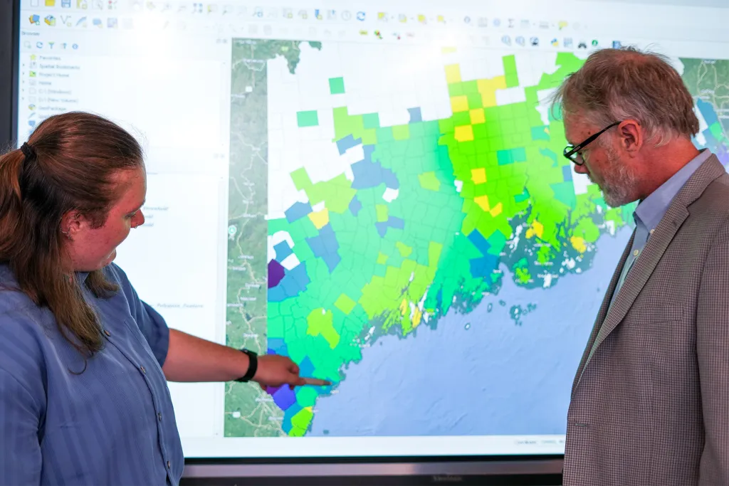 Ruth Ellis (Environmental Science, ’25) pointing to a colorful GIS heat map of coastal Maine displayed on a large screen.