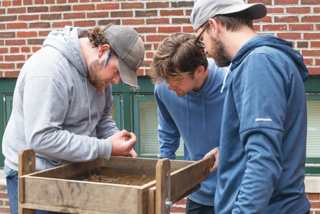 Three UNE students process dirt over the dig site