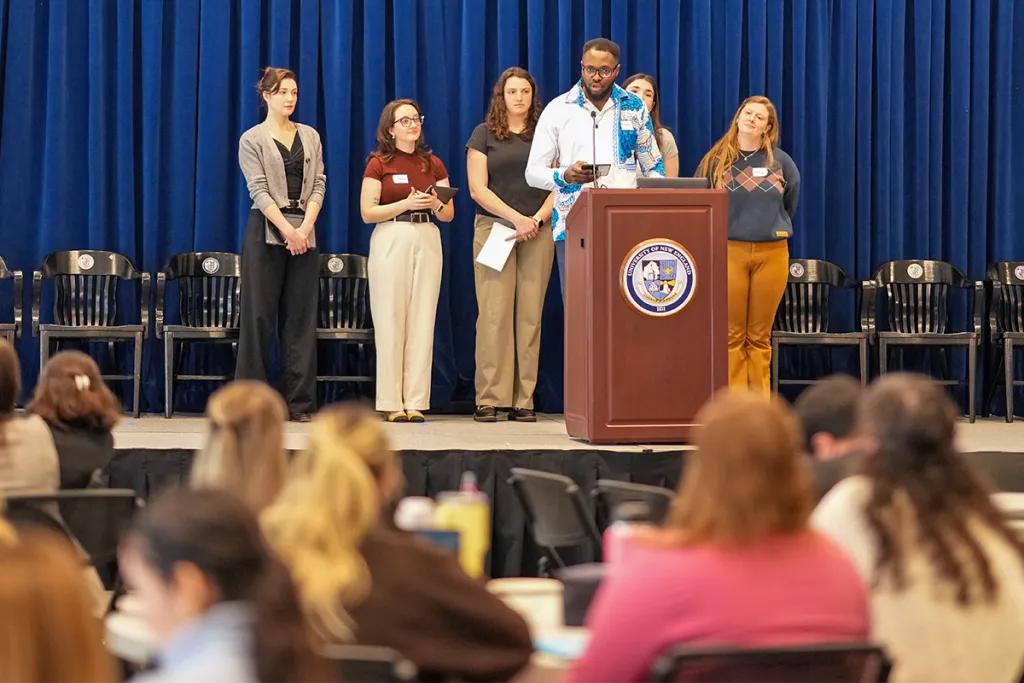 A group of UNE students present at a podium on stage before an audience during a Center for Public Health Practice and Maine AHEC event.
