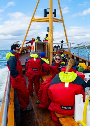 Several U N E students in cold-weather gear sit on a boat in the ocean off Iceland