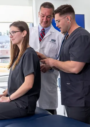 Two P A students practice using a stethoscope under a professor's supervision