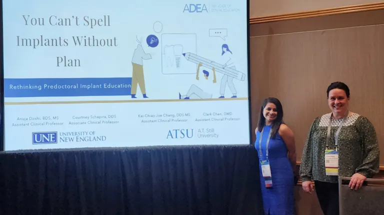 A student and faculty member pose in front of a slide deck on a large screen