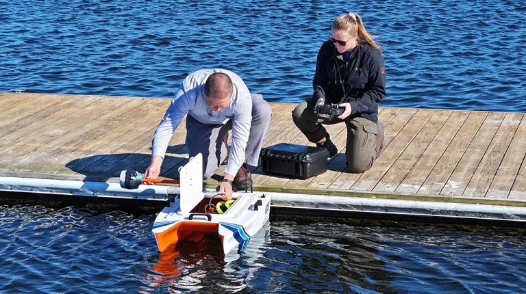 Two students send a small, robotic boat into the ocean for data collection