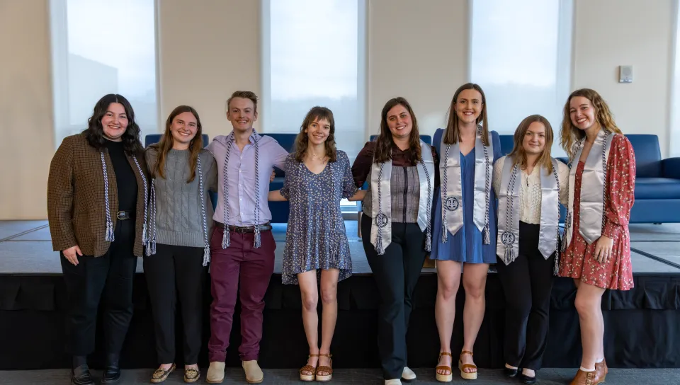 Graduating seniors pose for a group photo wearing their cords and stoles