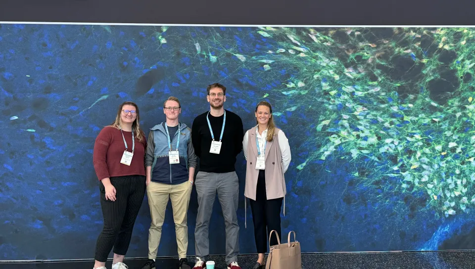 A group of UNE researchers pose in front of a wall with the Society for Neuroscience logo