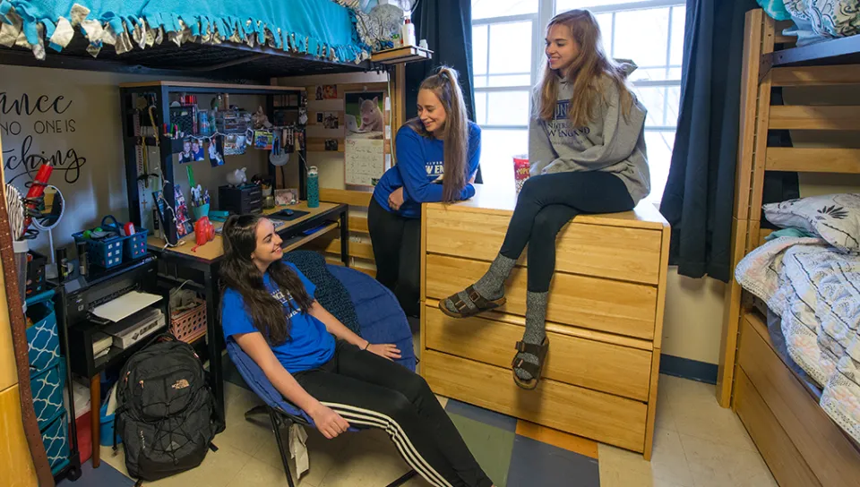 Three students laugh with each other while sitting in their U N E dorm
