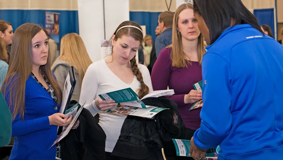A group of students review marketing materials from a business at a career fair