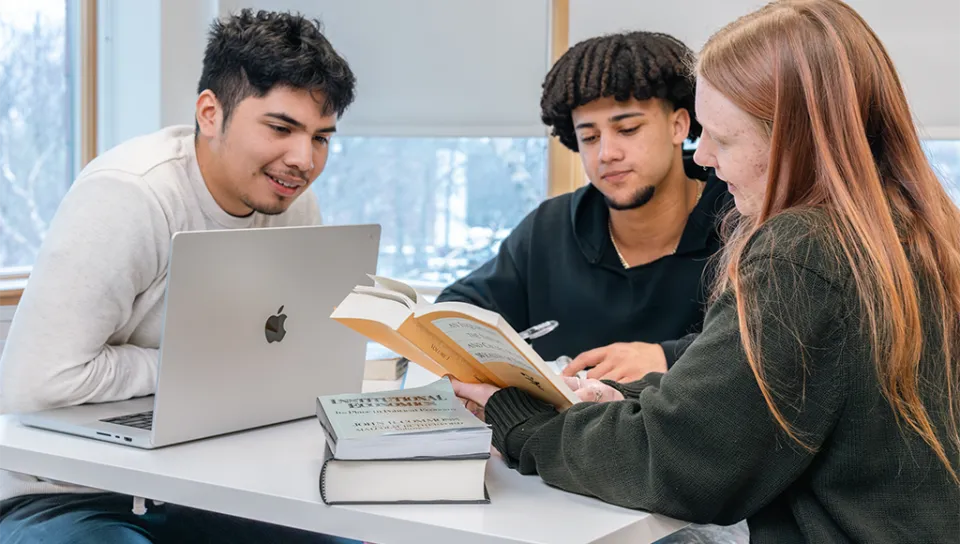A group of three students studying at a table together with a laptop and books