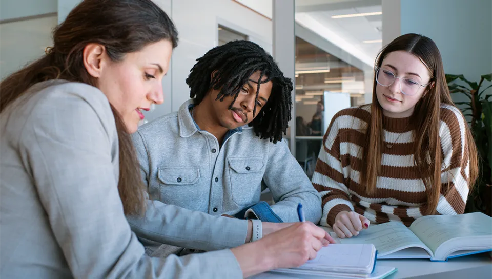 A professor writes in a notebook as two students look at the writing