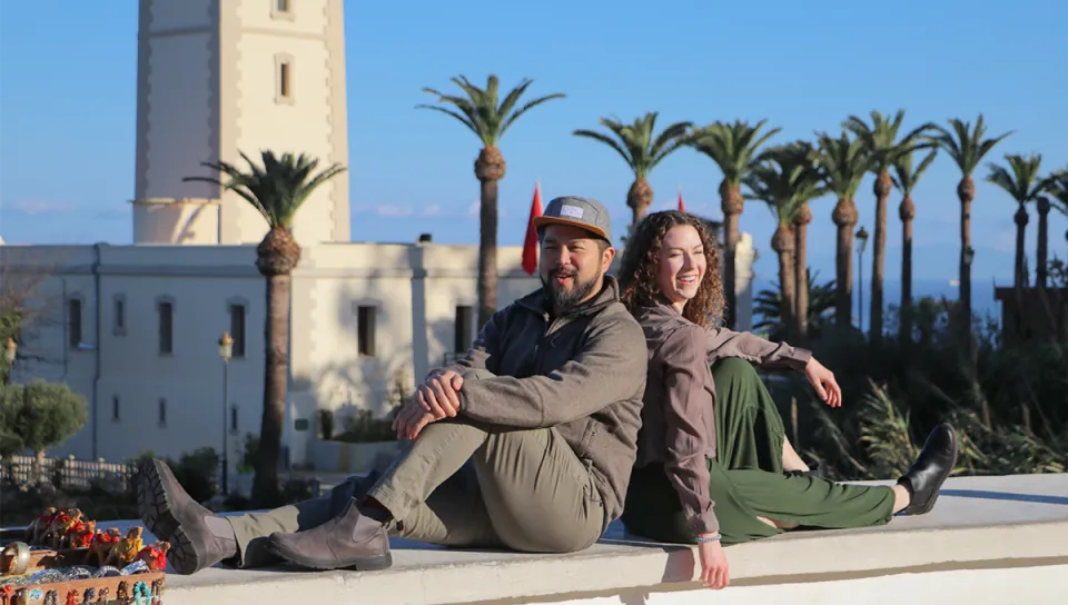 Two students pose together on a balcony in front of palm trees and a Moroccan tower