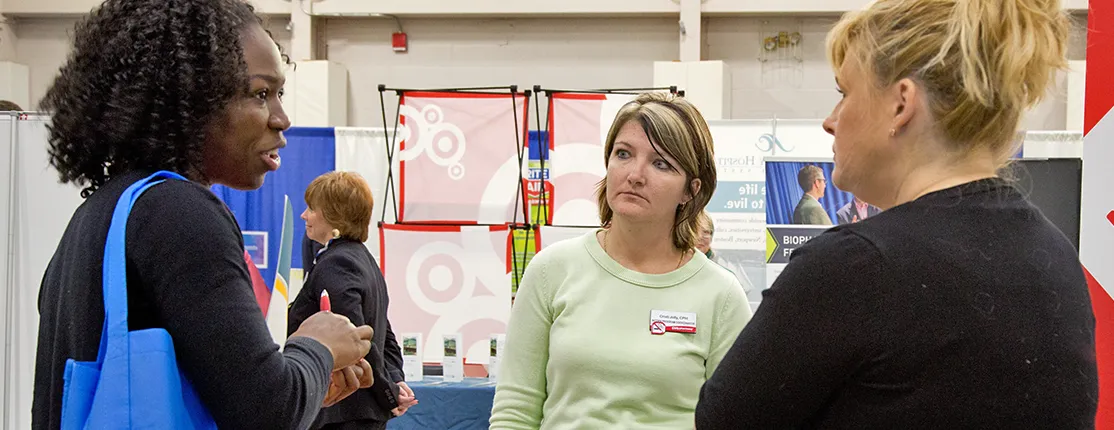 A students speaks with two representatives for a large business at a U N E Career Fair