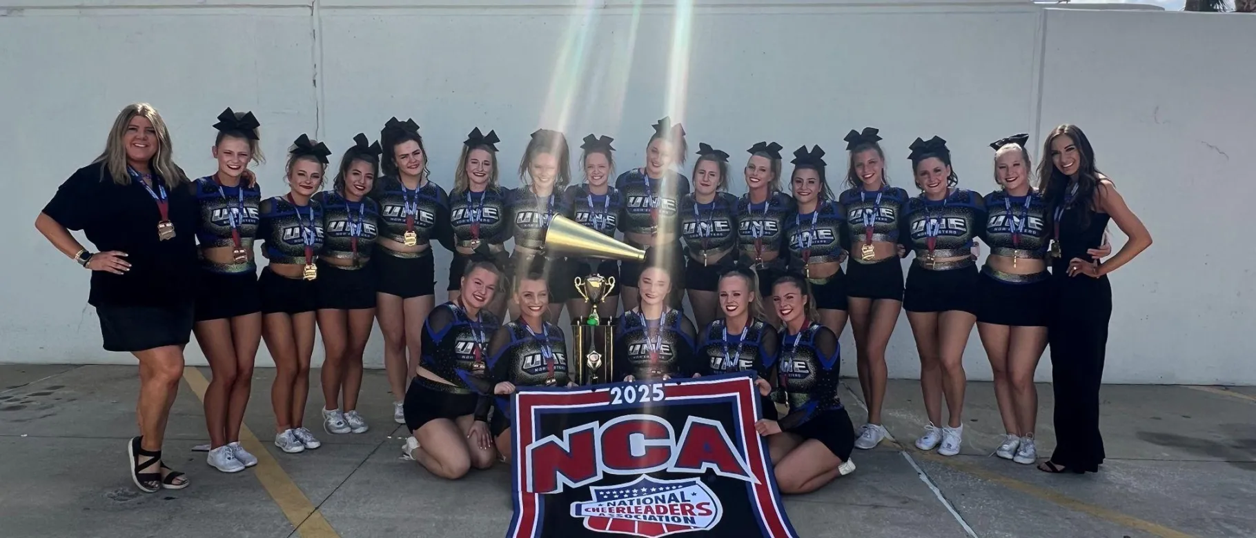 UNE cheer team members pose holding their championship trophy