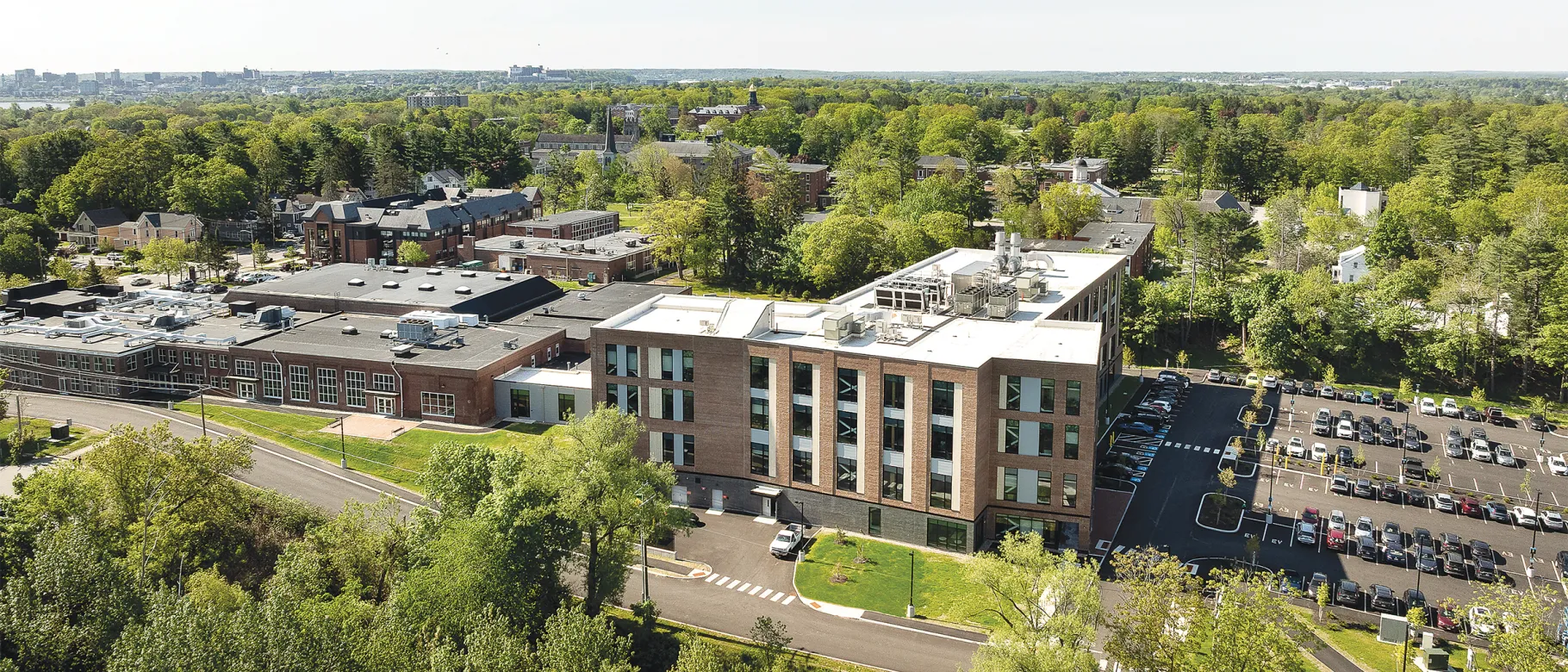 Aerial view of modern brick UNE health sciences campus building surrounded by trees and parking lots.
