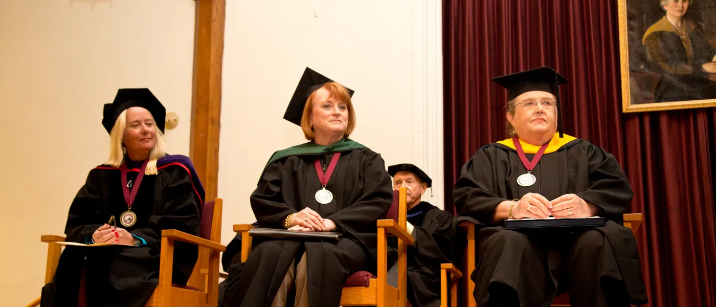 Three Debora Morton Society recipients sit in caps and gowns during convocation 