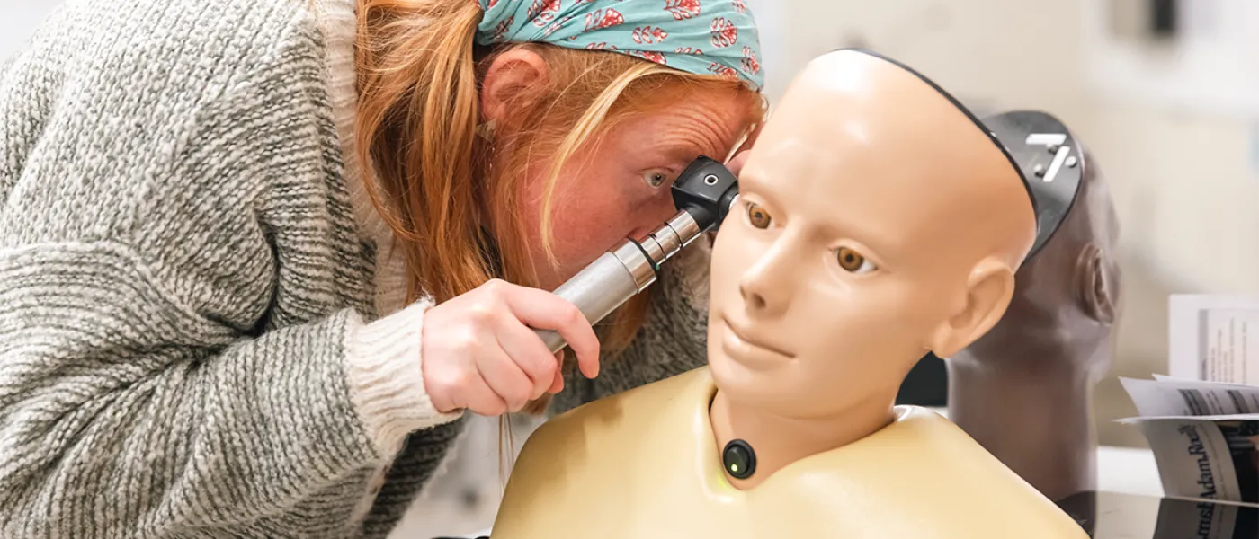 A nursing student tries peering into the ear of a patient simulator head with an otoscope