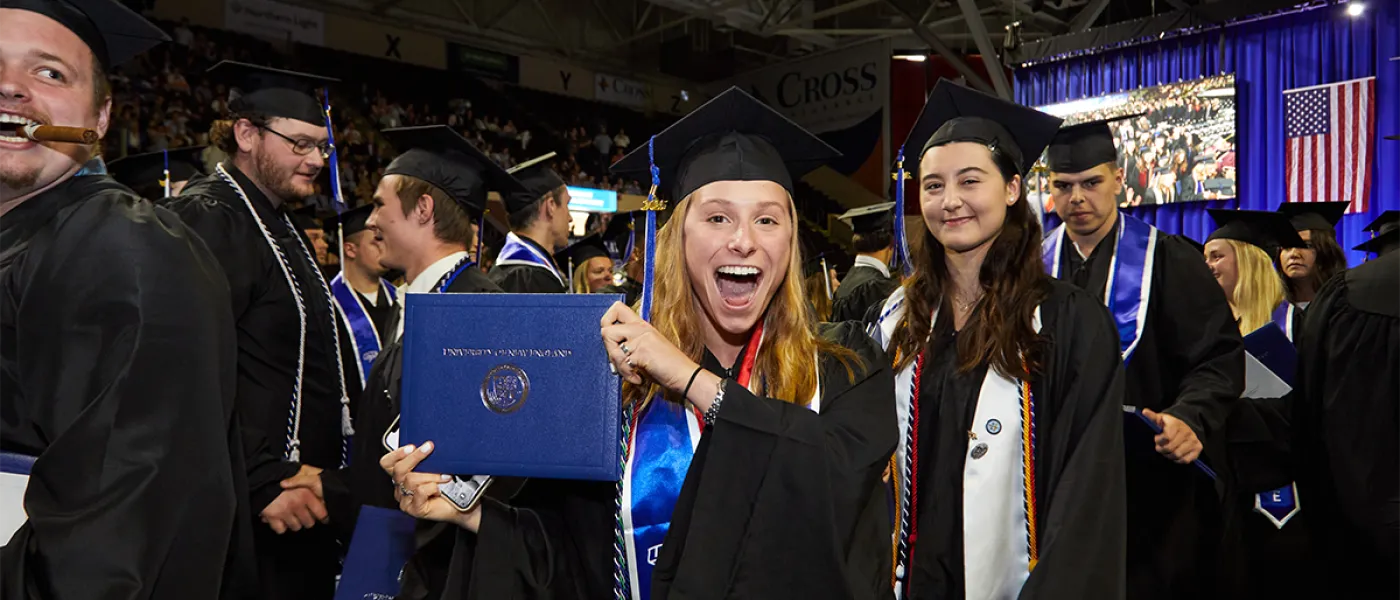 A student excitedly holds up their degree from the student crowd at Commencement