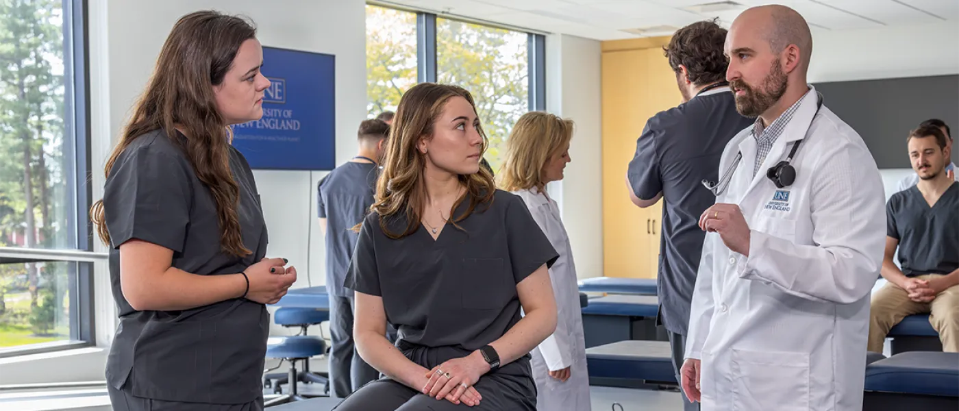 A professor talks to two physician assistant students during a skills lab