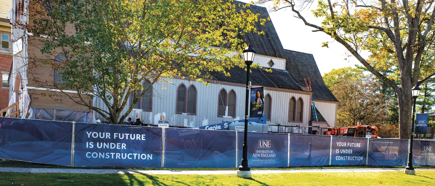 Exterior of Ludcke wrapped in protective sheeting behind construction fencing with UNE banners reading "Your Future Is Under Construction."