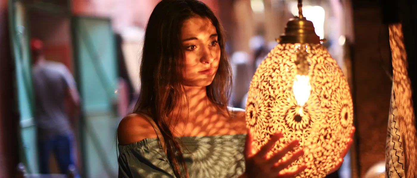 Student examines illuminated decorative lantern in evening market setting with blurred pedestrians in background.