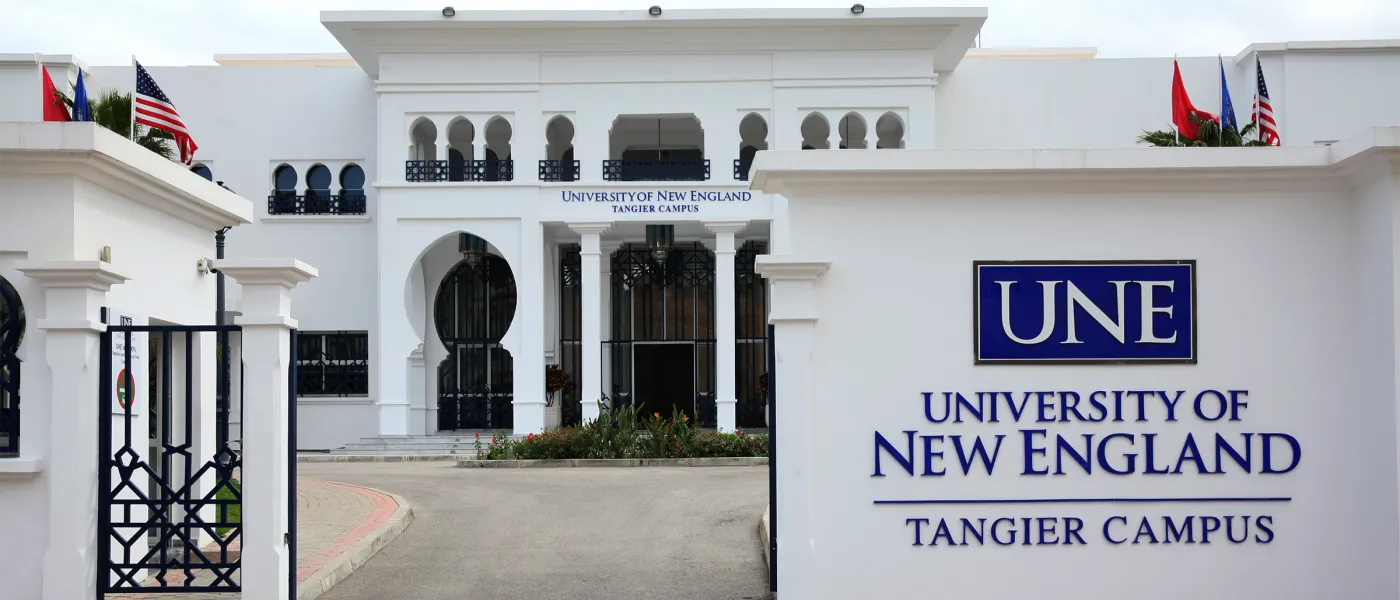 Main entrance to University of New England Tangier Campus showing white building facade with Moroccan architectural details, arched doorways, and UNE signage.