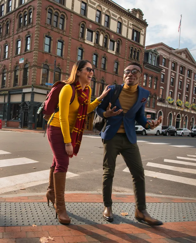 Two students walking across the street with brick buildings in the background
