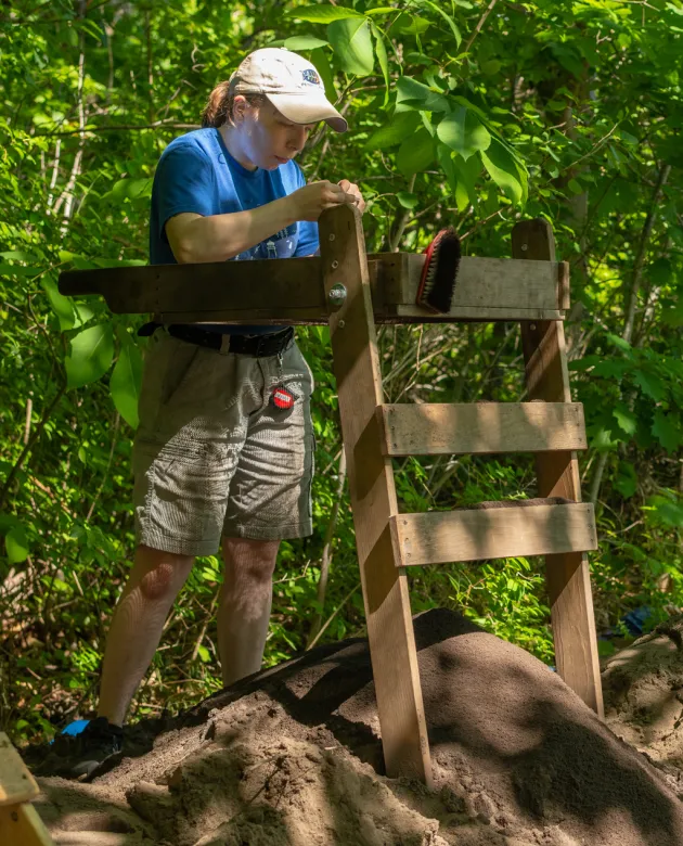 A student stands at a sifting table above a dig site