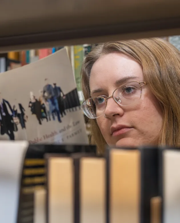 A student reading a book amongst library stacks